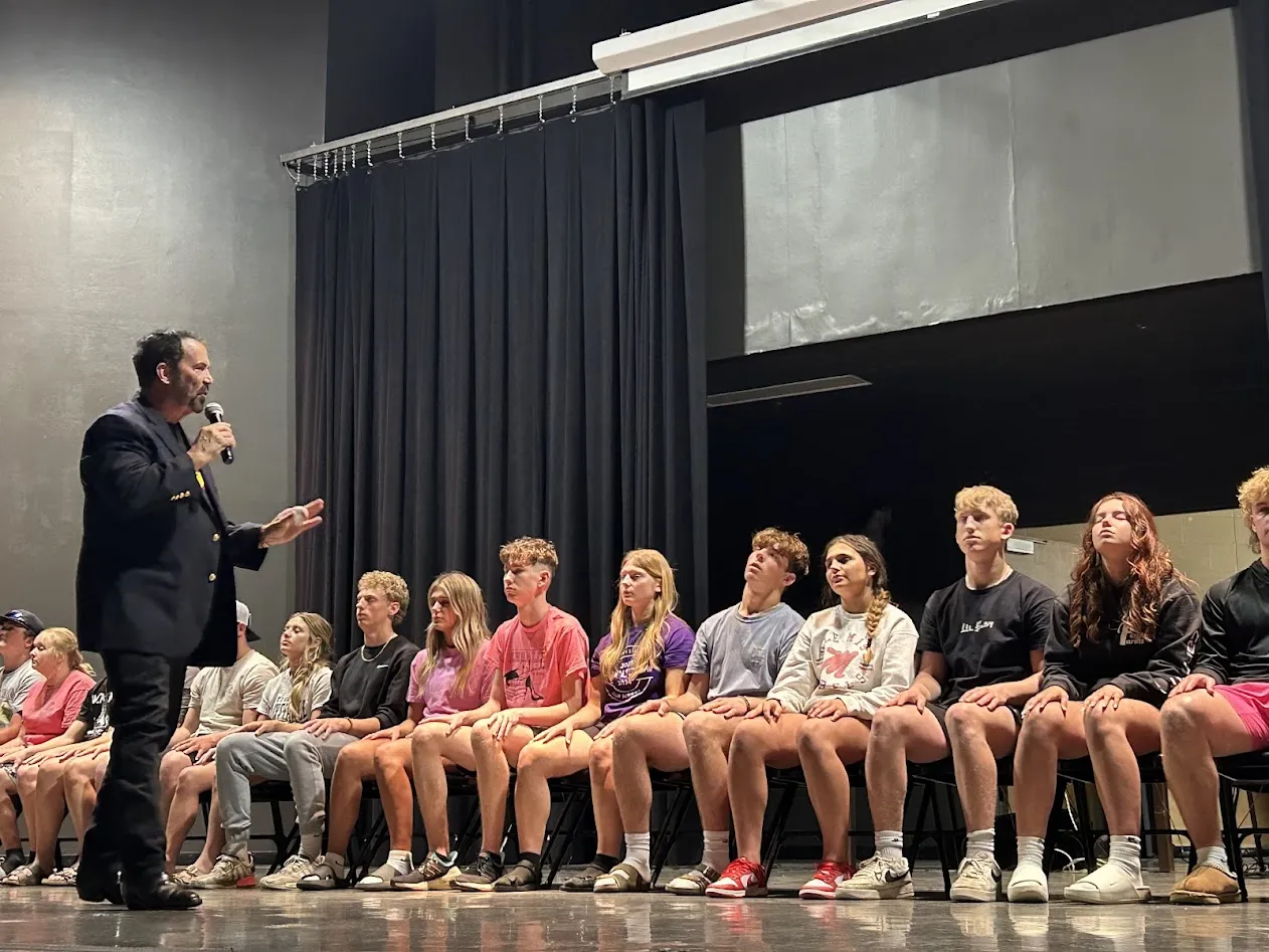 Hypnotist performs with high school students seated on stage during an engaging demonstration.