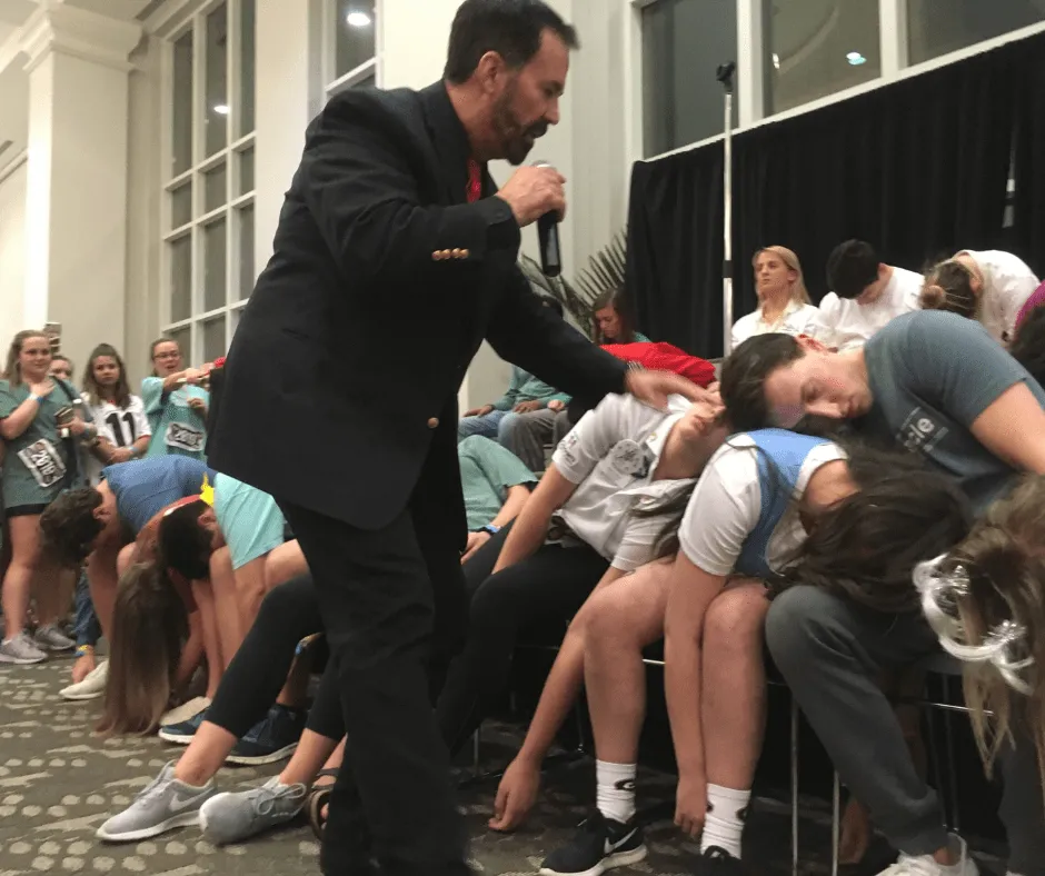 Hypnotist conducting a live show with participants appearing to be in a trance on stage.