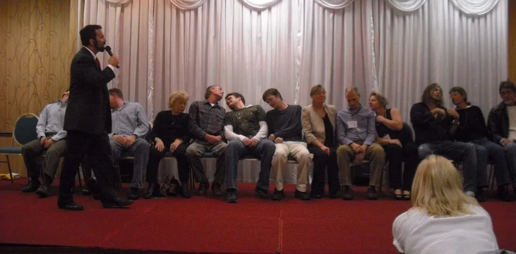 Hypnotist engaging a group of volunteers in hypnosis during a live stage show, with participants seated in a trance-like state.
